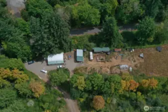 Parking area, 2 cargo containers with industrial roof spanning space between, the shed quarters, a cargo container with electricity and a "bedroom" with garden area in front, greenhouse. The line of trees indicates the creek.