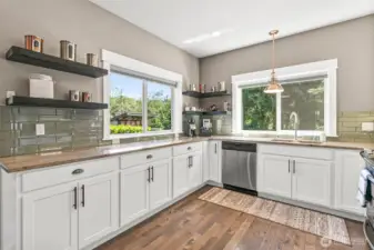 The kitchen features expansive counter space & custom cabinetry with a rustic flair to the floating shelves all while overlooking the lush backyard.