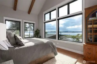 Wake up to the splendor of the Puget Sound in this luxurious primary ensuite, where expansive windows not only bring the outside in but frame the breathtaking water views as your own personal masterpiece. Vaulted ceilings with exposed beams rise above, creating an airy, open sanctuary that's as soothing as it is stylish. Here, comfort and elegance coexist effortlessly, ensuring every morning feels like a rejuvenation and every night is a tranquil retreat from the world. With the press of a button, the Hunter Douglas privacy shades descend for ultimate privacy.
