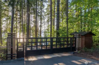 The grand security gate entry to the private waterfront estate, offering a glimpse into a secluded and luxurious retreat. The robust, elegant custom designed gates stand as a promise of privacy and exclusivity, opening to reveal a lush, tree-lined drive that leads directly to the water's edge. This entryway sets the tone for a prestigious and serene living experience.