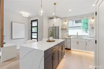 The island anchors the kitchen with its striking white marble surface and rich dark cabinetry, offering both a visual centerpiece and a functional hub for cooking, gathering, and casual dining.