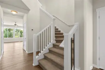 Welcoming entry way with carpeted stairs, elegant white trim and a view to the bright living area with large windows.