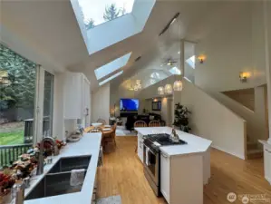 Open concept kitchen and family room featuring vaulted ceilings and three new extra large skylights and a bright loft overlooking the space that includes two additional new skylights - creating a spacious, airy, and connected living area perfect for both everyday life and entertaining.