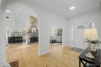 Light-Filled Foyer With Arched Openings  Step into a bright, welcoming foyer featuring wide-plank hardwood floors, soft neutral tones & elegant arched openings that frame the main living spaces. Recessed lighting & abundant natural light create an airy first impression, while sightlines to the stone fireplace, kitchen & living room highlight the home’s open yet thoughtfully defined layout.