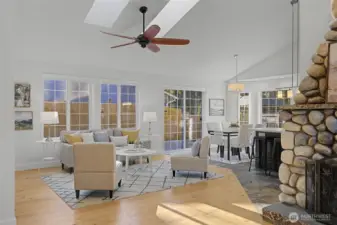 The vaulted great room is filled with natural light from multiple skylights and a wall of windows, creating a bright, open gathering space. Warm wood floors, a modern ceiling fan and inviting seating area frame views of the backyard through sliding glass doors that open to the composite deck. The space flows effortlessly into the dining nook and kitchen, making it ideal for both relaxed daily living and entertaining.