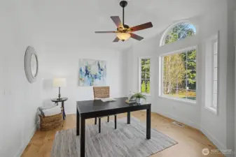 This serene, sunlit room works beautifully as a home office or formal dining space. An elegant arched transom window and tall side windows fill the room with natural light, while warm wood floors and soft neutral finishes create a calm, inviting atmosphere. A ceiling fan adds year-round comfort, making this an ideal setting for remote work, creative projects or intimate gatherings.