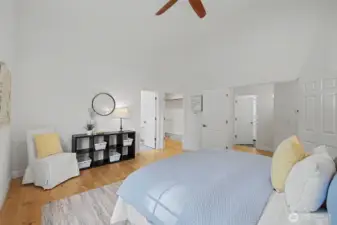 Spacious primary bedroom featuring vaulted ceilings, warm wood flooring and a soft neutral color palette that enhances the room’s light, open feel. Generous wall space easily accommodates a king-size bed and additional furnishings, while the open layout creates a sense of calm and flexibility. The walk-in closet and adjacent hallway access are thoughtfully positioned just off the bedroom for everyday convenience