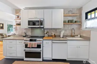 A beautiful kitchen has been fully remodeled to the studs and joists. Custom white cabinetry with vintage hardware, quartz countertops, Moroccan tile backsplash, Cafe' appliance package, open Douglas fir shelving, and Marmoleum flooring accent this space so well. There is also an Insinkerator garbage disposal and no-edge sink.