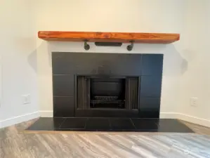 A close-up view of the fireplace with its single stained wood mantel and chunky matte black hardware creates a striking focal point in the great room, adding both warmth and a touch of modern style to the space.