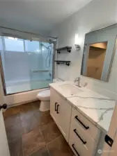 The primary bath has been updated with a modern vibe, featuring sleek slab quartz, crisp white tile, and black fixtures. A window in the full shower/tub combo allows natural light to flood the space while maintaining privacy.