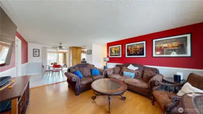 Spacious living room with warm wood-style flooring, a bold accent wall, and an open connection to the dining area and kitchen.