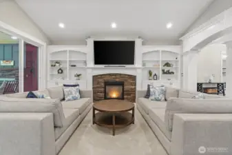 Stunning built-in shelves and cabinets flank the gas fireplace, creating a beautiful focal point in the great room. They perfectly complement the wood-wrapped pillars, detailed millwork, and graceful arched doorways, delivering a cohesive and refined aesthetic throughout the space.