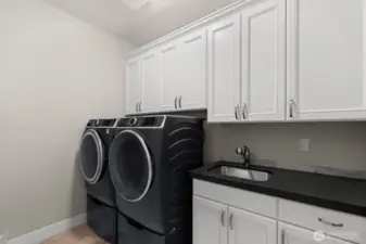 A large laundry room includes upper and lower cabinets, washer and dryer and a utility sink.
