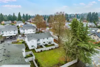 This aerial view shows off the home's location overlooking a grassy area, with mature trees all around.