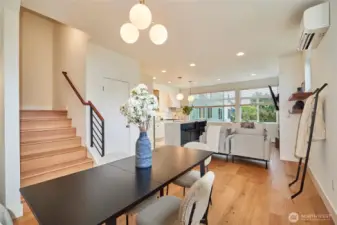 A look from the dining area to the living room and kitchen. Note the oak hardwoods, ductless split heat/AC, wall of windows and designer finishes.
