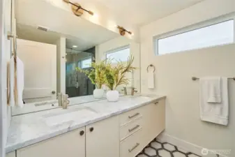 A look at the "spa-like" primary bathroom with quartz countertops, 2 undermount sinks, Grohe faucets, tile floor, West Elm lighting and tile shower surround with both rainfall and hand held shower heads.