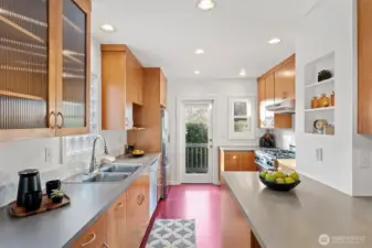 Full of natural light and classic charm, the kitchen features  Marmoleum flooring, glass-fronted cabinets, and both a leaded glass door to the dining room  and a glass-paned door to the backyard. Modern updates include a Bosch dishwasher, Fisher &  Paykel fridge, Décor gas range, and Allure hood vent. Step right out to the back deck and  tiered yard—perfect for morning coffee or summer dinners al fresco.