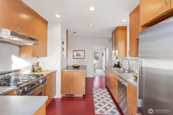 Full of natural light and classic charm, the kitchen features  Marmoleum flooring, glass-fronted cabinets, and both a leaded glass door to the dining room  and a glass-paned door to the backyard. Modern updates include a Bosch dishwasher, Fisher &  Paykel fridge, Décor gas range, and Allure hood vent. Step right out to the back deck and  tiered yard—perfect for morning coffee or summer dinners al fresco.