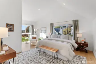 The primary bedroom on the upper level with cathedral ceilings and large new windows frame views of downtown and the evening sky, filling the room with golden light. From sunrise to sunset, it’s a peaceful retreat  that feels timeless— high above the tiered gardens below.