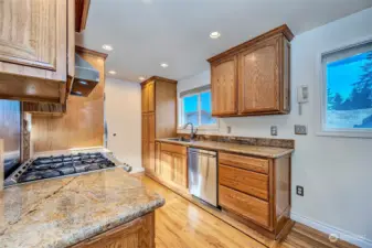 Kitchen with slab granite counters, gas cook top stove with a convectional electric oven and newer stainless steel appliances and hood fan.