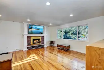 Bright cheery Living room with a brick, wood burning fire place and recently refinished oak hard wood floors.