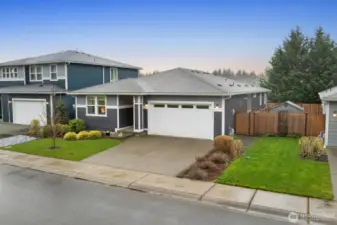Angled exterior perspective highlighting the rambler-style home with front porch entry, attached garage, manicured lawn, wood privacy fencing, and neighboring homes in the Bonney Lake Falling Water neighborhood.