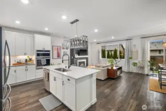 Spacious kitchen and living area with a large island sink, modern pendant light fixture, stainless steel appliances, recessed lighting, and sliding glass door access to the backyard patio.