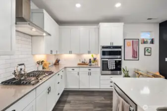 Detailed kitchen angle featuring stainless steel gas cooktop, subway tile backsplash, under-cabinet lighting, white cabinetry, and a center island with sink and additional seating space.