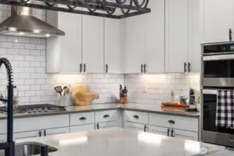 Detailed kitchen view highlighting white shaker-style cabinetry, subway tile backsplash, stainless steel wall ovens, and extended counter space along the L-shaped layout.