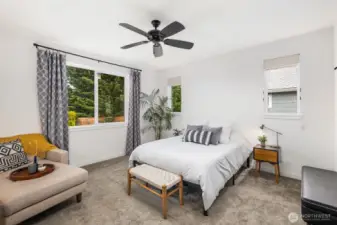 Spacious bedroom with large windows bringing in natural light, ceiling fan overhead, and comfortable layout with space for both sleeping and seating.