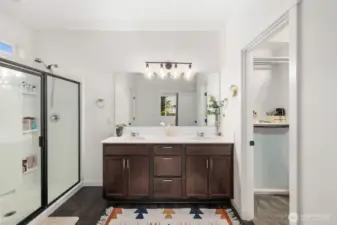 Primary bathroom with dual sink vanity, large mirror, modern lighting fixture, and glass-enclosed shower alongside a walk-in closet entrance for added convenience.