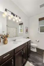 Another view of the bathroom highlighting the long vanity counter, warm wood cabinetry, and bright mirror lighting that makes the room feel open and welcoming.