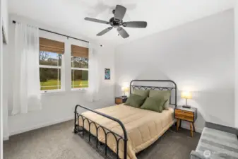 Comfortable secondary bedroom with large windows bringing in natural light, ceiling fan overhead, and peaceful outdoor views that make the room feel bright and relaxing.