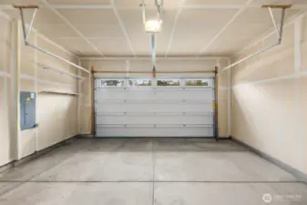 Spacious attached two-car garage with overhead door, built-in shelving for storage, and room for vehicles, tools, or outdoor gear.
