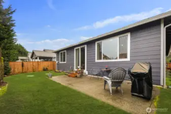 Outdoor patio area with room for seating and grilling, surrounded by lawn and garden beds, offering a comfortable place to enjoy warm Bonney Lake evenings.