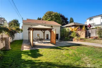 A large grass yard is just off the patio. To the right is the driveway leading to the attached garage.