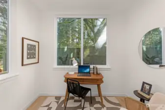 The ultimate work-from-home setup! This sun-filled den invites creativity and focus, surrounded by peaceful greenery visible through expansive windows—a space designed for productivity.