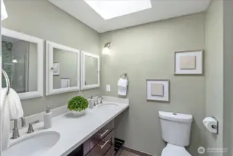 Primary en-suite bathroom with dual sinks, walk-in shower, quartz counter tops & a skylight