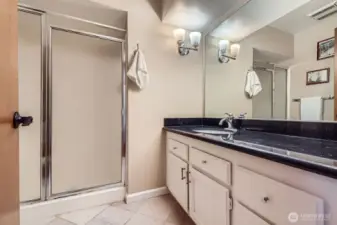 Dressed to impress, the ¾ hall bathroom has a stylish black slab granite counter, white vanity, and grey & white travertine tile floors.