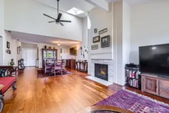 The open-concept living and dining spaces feature a stately travertine-surround fireplace, skylight, and a modern fan.
