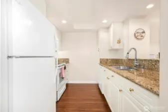 Updated galley kitchen with granite counters, white cabinetry, and recessed lighting including new appliances.