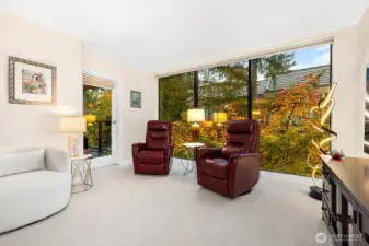 The inviting living area features expansive picture windows showcasing stunning golden hour views of the surrounding trees, filling the space with warm natural light.