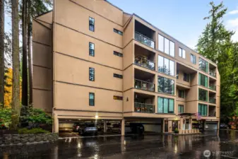 Building exterior showcasing large windows and covered balconies set against forest surroundings.