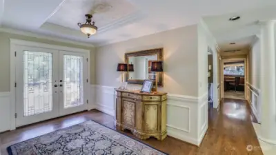 Leaded glass doors open to entry foyer featuring rich hardwood floors, formal white millwork and custom ceiling detail.