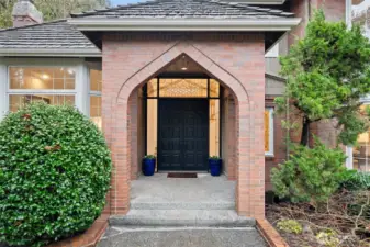 Inviting covered entry with architectural brick archway, custom double doors, and warm interior glow—setting the tone for refined craftsmanship and a welcoming arrival.
