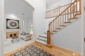 Bright, welcoming foyer featuring hardwood floors, soaring ceilings, and a classic wood staircase—creating a grand yet inviting first impression.