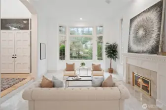 A stunning view of the living room showcasing the gas fireplace, bay-style windows overlooking lush greenery, and an open flow to adjacent living spaces.