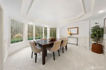 Elegant dining room featuring a tray ceiling, classic wainscoting, and expansive windows that frame lush greenery—an inviting space designed for memorable gatherings and refined meals.