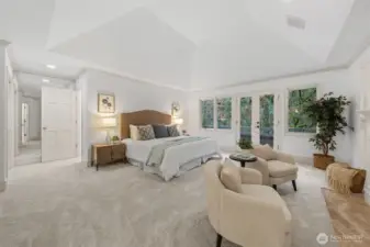 An expansive and serene Primary Suite showcasing soaring vaulted ceilings, plush new carpet, and fresh paint. Generous proportions easily accommodate a sitting area, while large windows and a private exterior door fill the room with natural light and tranquil, tree-lined views. To the back left is the walk-in closet.