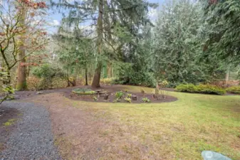 A peaceful, park-like backyard setting surrounded by mature evergreens and natural landscaping. Meandering paths, open lawn space, and established plantings create a serene outdoor retreat with plenty of room to relax or explore.